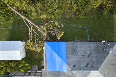 Aerial view of damaged in hurricane Ian house roof covered with blue protective tarp against rain water leaking until replacement of asphalt shingles.